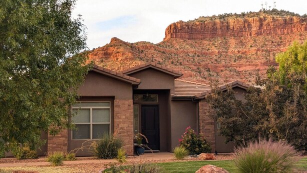 A modern house with a stone facade, a dark front door, and a well-maintained front yard with various plants and a large rock.