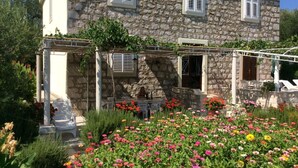 Um edifício de pedra com área externa coberta para sentar e um jardim com flores coloridas.