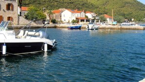 Uma marina com barcos atracados, um edifício de pedra com telhado vermelho e uma colina ao fundo.