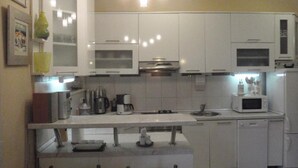 Una cocina compacta con armarios blancos, microondas, cafetera y lavabo.