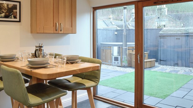 A dining area with a table set for four, wooden cabinets above, and a sliding glass door leading to a backyard with a wooden fence and a small patio.
