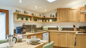 A modern kitchen with wooden cabinets, a dining table with chairs, a built-in dishwasher, and a skylight.