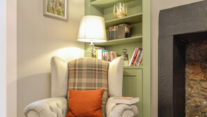 A cozy armchair with a plaid cushion, a bookshelf with books, a lamp, and a fireplace.