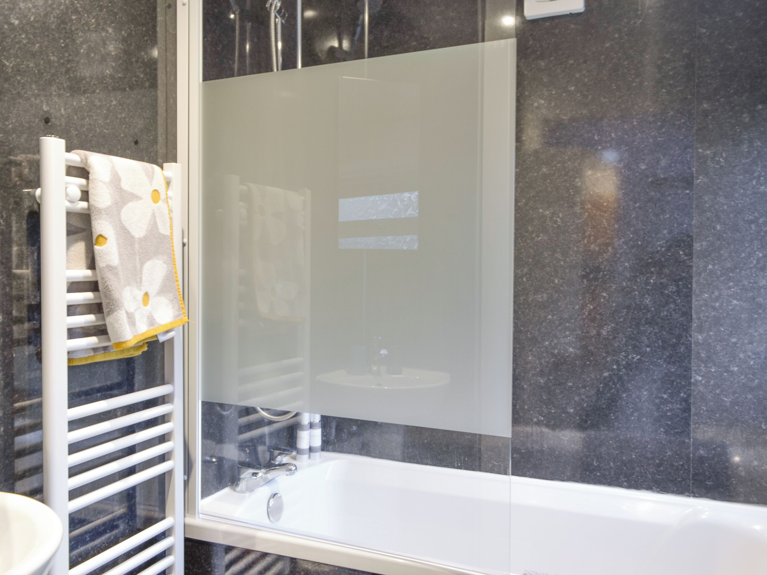 A bathroom with a glass-enclosed shower, a white sink, and a towel rack with a patterned towel.