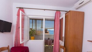 A room with a bed, a TV, a table with a red tablecloth, a wooden wardrobe, and a window with pink curtains. - Triple Room with Private Balcony (Brist)