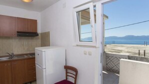 Eine kleine Küche mit Kühlschrank, Holzschränken und einem Fenster mit Blick auf einen Strand.