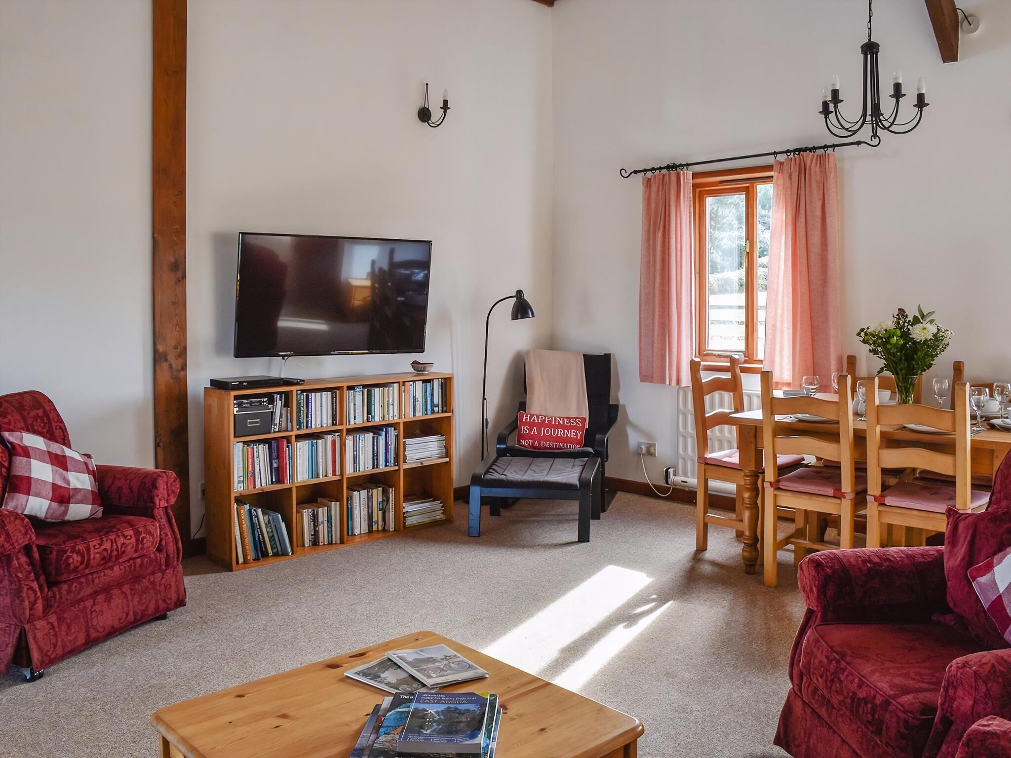Una sala de estar con televisión, estanterías, un sofá rojo, una mesa de centro de madera y una zona de comedor con mesa y sillas.