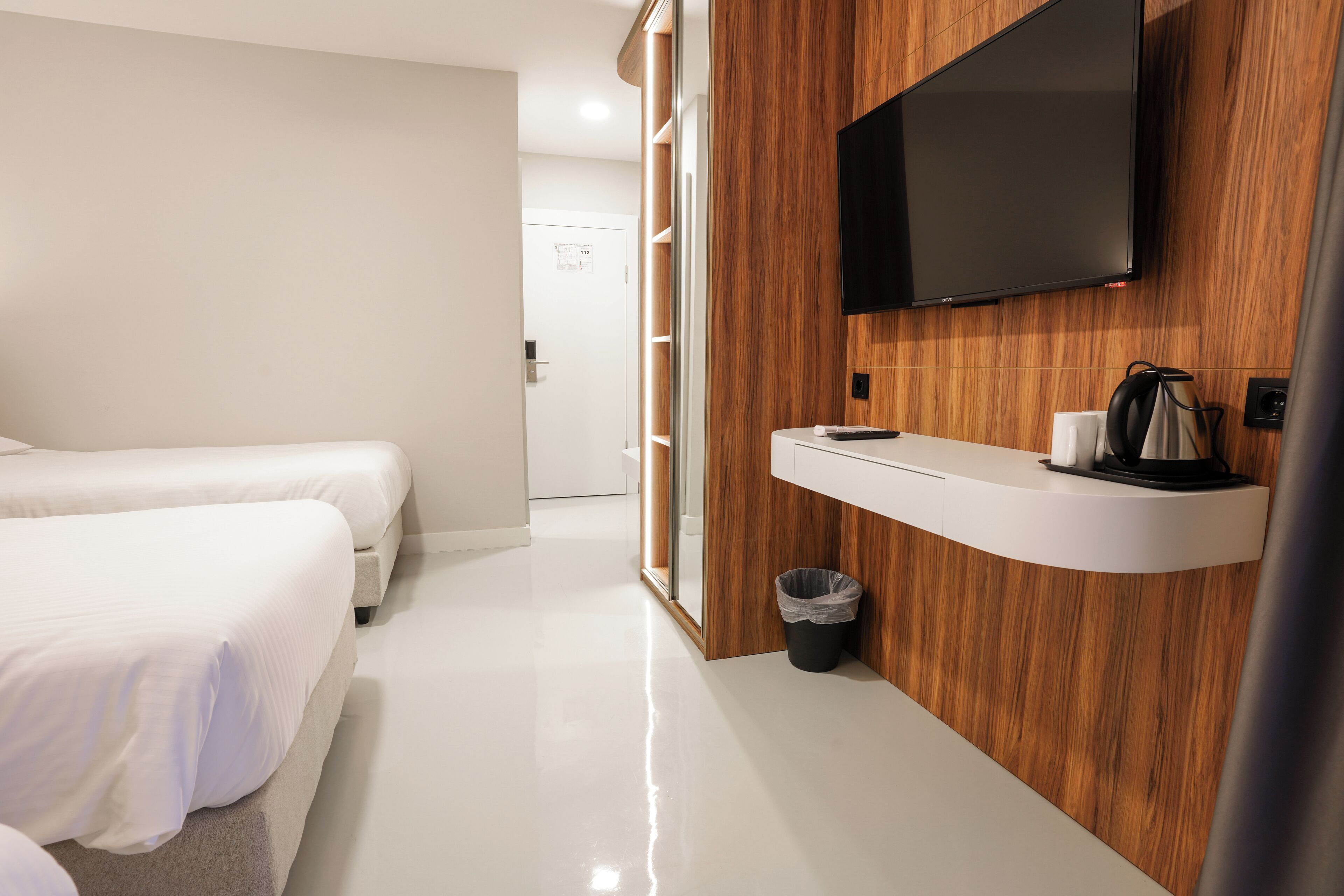 Habitación de hotel con dos camas, una pared decorativa de madera, un televisor montado y una pequeña zona con lavamanos.