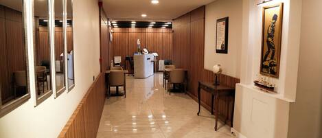 A hotel corridor with wooden paneling, a reception desk, and several seating areas.