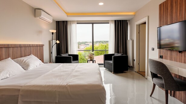 Ein Hotelzimmer mit einem großen Bett, einem Fernseher, einer Sitzecke mit zwei Sesseln und einem Balkon mit Blick.
