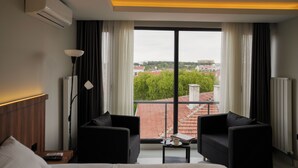 Ein modernes Hotelzimmer mit großem Fenster, zwei schwarzen Sofas, einem kleinen Tisch und einem Bett.