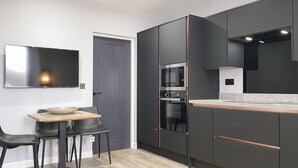 A modern kitchen with dark cabinetry, a built-in oven, and a dining area with a wooden table and chairs. - 1 bedroom accommodation in Anstruther (Anstruther)
