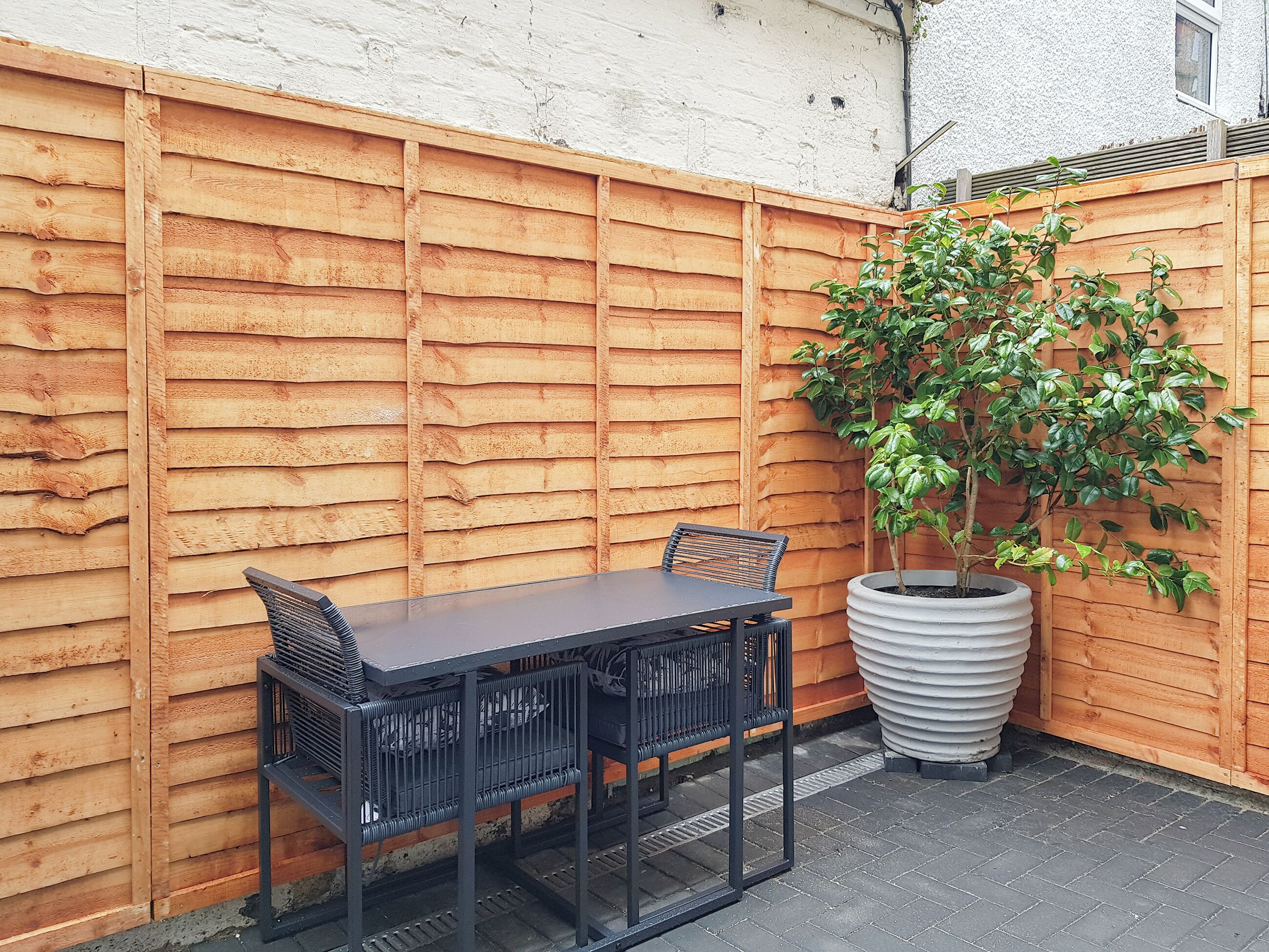 A patio area with a wooden fence, a table with chairs, and a potted plant.