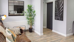 A modern living room with a brown leather sofa, a large mirror, a potted bamboo plant, and a wooden floor. - 1 bedroom accommodation in Anstruther (Anstruther)