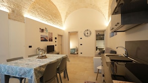 A compact kitchen with a dining area, featuring a clock, a grill, and a tiled floor. - La Casetta (Mola di Bari)