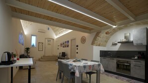 A spacious dining area with a high ceiling and exposed beams, a kitchen with modern appliances, and a cozy seating arrangement. - La Casetta (Mola di Bari)