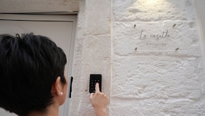 A person using a wall-mounted device, possibly a doorbell or intercom, with a sign above it reading "La casetta" and a phone number. - La Casetta (Mola di Bari)