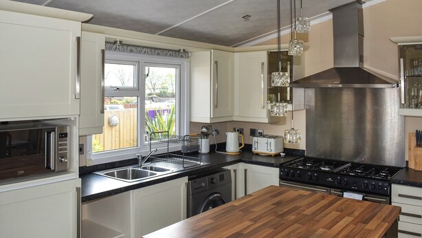 A modern kitchen with white cabinets, a wooden countertop, a stainless steel range hood, and a window with a view of the outside. - 2 bedroom accommodation in Towyn (Towyn)