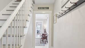 A hallway with a staircase, a 'Welcome Aboard' sign, a coat rack, and a dining area in the background. - Maine Getaway with Stunning Water Views-Kayak, SUP, & More! (Kennebunk)