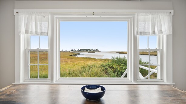 A room with a large window offering a view of a coastal landscape. - Maine Getaway with Stunning Water Views-Kayak, SUP, & More! (Kennebunk)