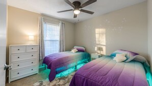 Ein Schlafzimmer mit zwei Betten, einem Deckenventilator, einem Schminktisch und einem Fenster mit Jalousien.