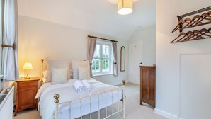 A bedroom with a bed, bedside lamp, window with curtains, wooden wardrobe, and a hanging rack.