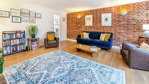 A living room with a blue sofa, a coffee table, a bookshelf, and a brick wall.