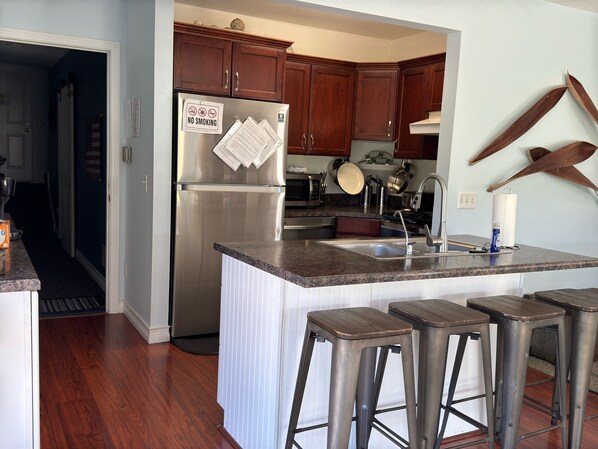 A modern kitchen with a stainless steel refrigerator, wooden cabinets, a granite countertop, a sink, and bar stools. - Eagle Isle Wings Spacious 8 bedroom Split Townhouse on the Sandusky River (Fremont)