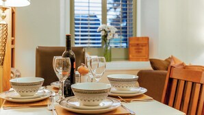 A dining table set with white and patterned bowls, wine glasses, and a bottle, with a window and blinds in the background.