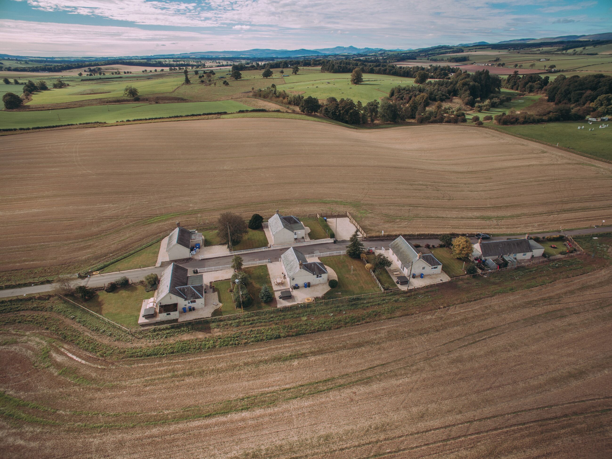 An aerial view of a rural property with multiple houses, a road, and surrounding fields.