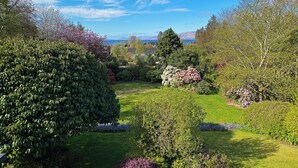 A well-maintained garden with various shrubs and flowering plants, a neatly trimmed lawn, and a clear view of the surrounding landscape. - Garden Flat - set in beautiful large garden with old church ruins on the grounds (Onich)