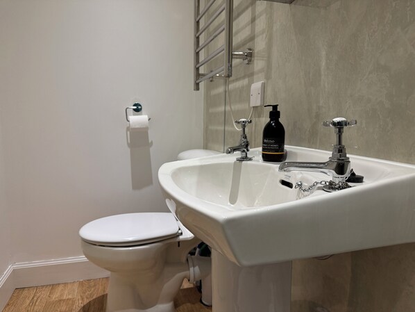 Un baño con inodoro blanco, lavamanos y espejo.