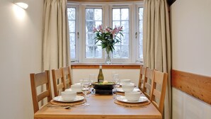 A dining table set for four with white plates, bowls, and glasses, a bottle of wine, and a vase with flowers. - 3 bedroom accommodation in Blairgowrie (Blairgowrie)