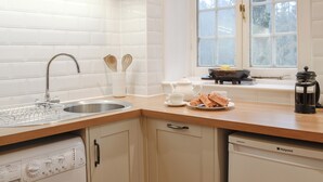 A modern kitchen with white cabinetry, a stainless steel sink, a built-in dishwasher, and a window with a view of trees. - 3 bedroom accommodation in Blairgowrie (Blairgowrie)