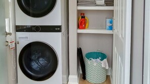 Une buanderie équipée de deux machines à laver superposées, d’étagères avec des vêtements pliés, d’une bouteille de lessive et d’un panier à linge.