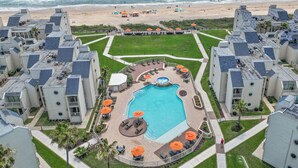 Un complejo residencial con piscina central, rodeado de zonas de descanso con sombrillas y vistas a la playa.