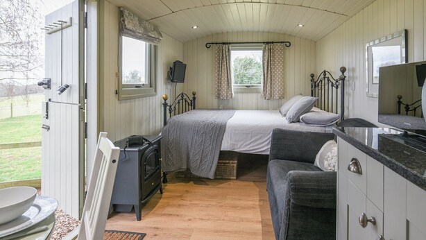 A cozy bedroom with a bed, a dresser, a television, and a window with curtains. - Hay and Hedgerow Glamping (Nordley, near Bridgnorth)