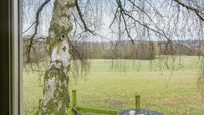 A view from a window overlooking a grassy field with a metal table and chairs, a tree with moss, and a wooden fence. - Hay and Hedgerow Glamping (Nordley, near Bridgnorth)