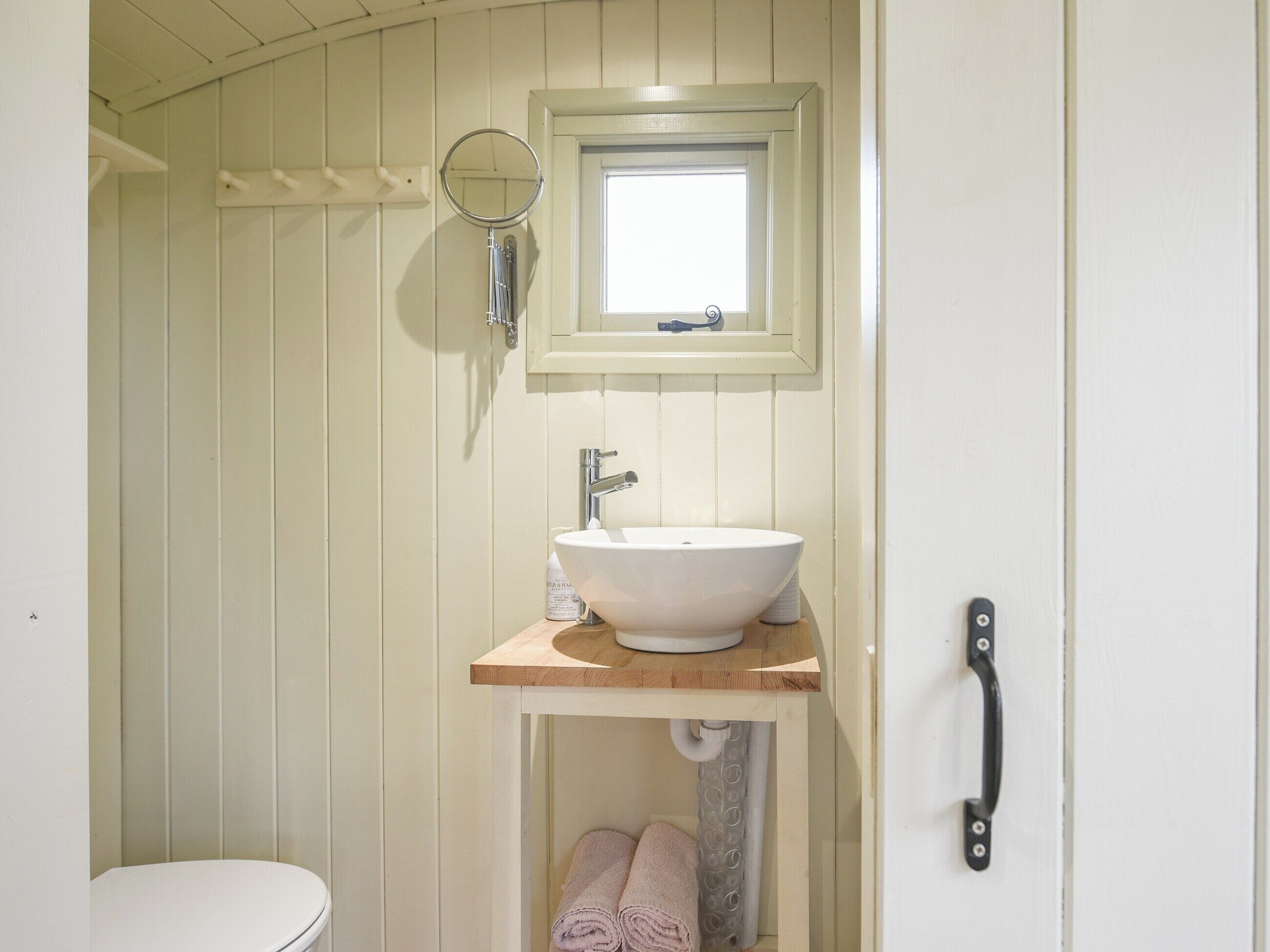 Un baño con inodoro blanco, tocador de madera con lavamanos blanco, espejo y toallero.