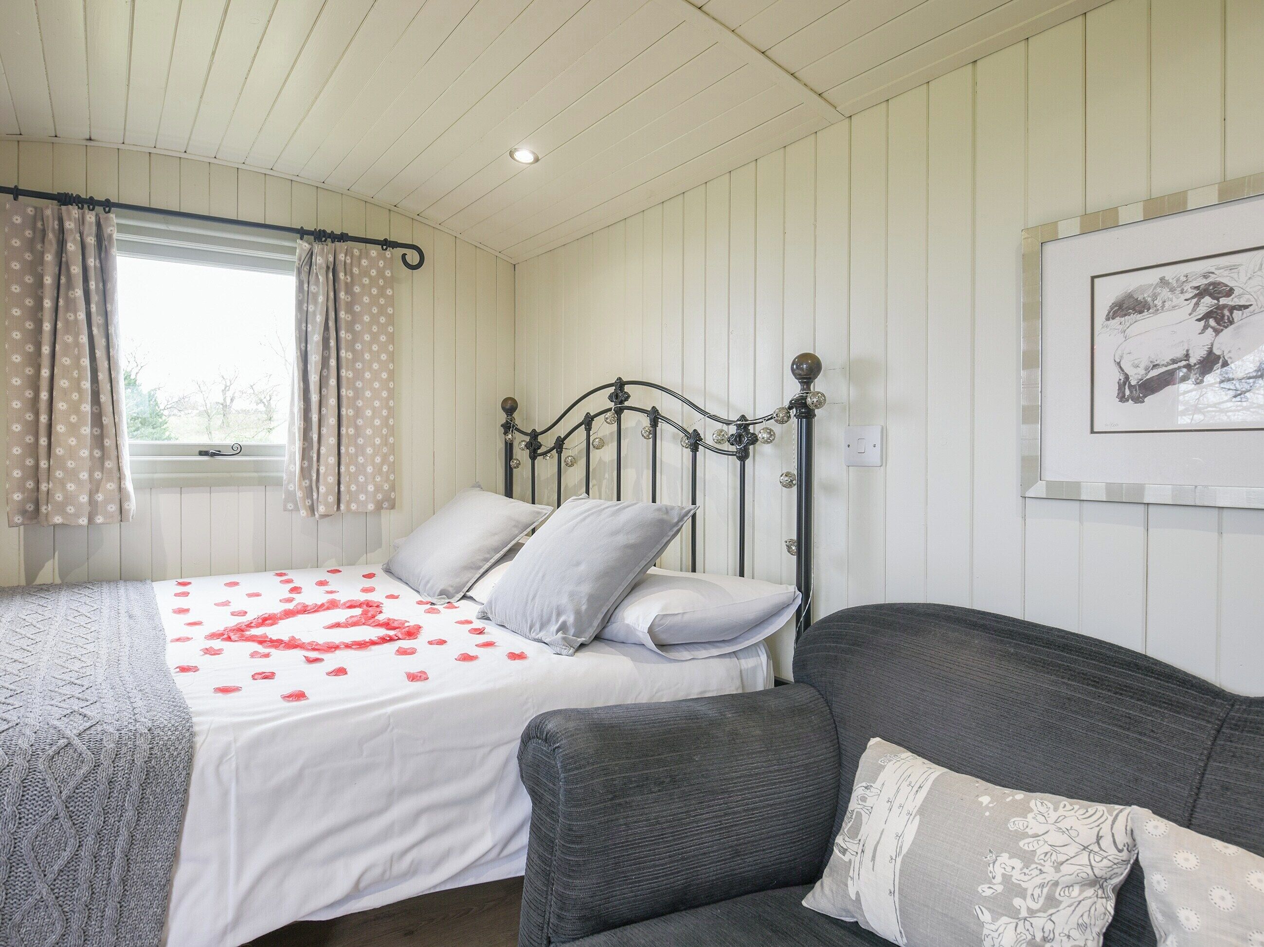 A bedroom with a bed, grey couch, and a framed picture on the wall.