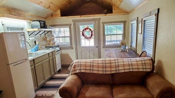 A cozy living room with a brown leather couch, a kitchen area with a refrigerator, microwave, and cabinets, and a door with a wreath. - Tunnel Mountain Getaways- Cozy Retreat with Scenic Views! (Elkins)