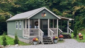 A small, single-story cabin with a porch, surrounded by a gravel driveway and potted plants. - Tunnel Mountain Getaways- Cozy Retreat with Scenic Views! (Elkins)