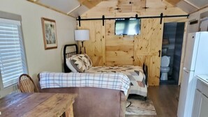 A cozy room with a bed, a wooden table, a lamp, and a refrigerator. - Tunnel Mountain Getaways- Cozy Retreat with Scenic Views! (Elkins)