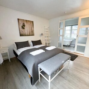 A bedroom with a bed, a bench, a ladder, and a bathroom visible through a glass door.