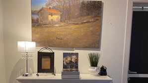 Une cheminée avec un feu allumé, un tableau encadré au-dessus, et une petite table avec une lampe et des objets décoratifs.