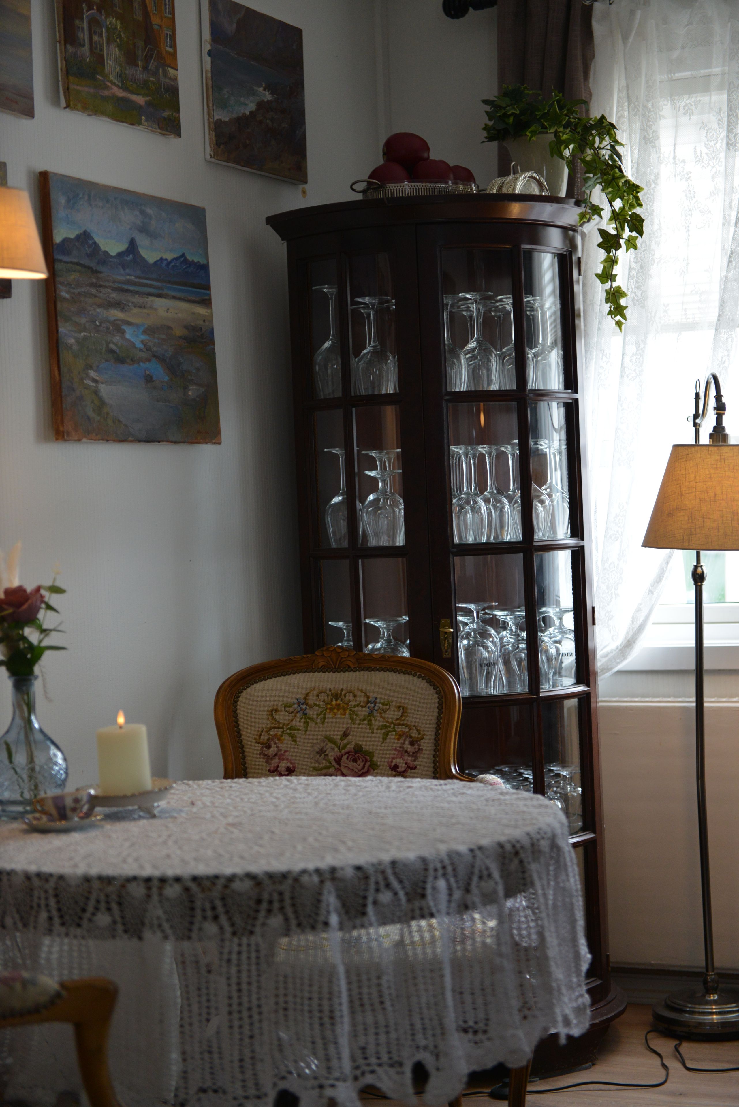 A dining area with a table set for two, a cabinet with glassware, and a chair with a floral pattern.