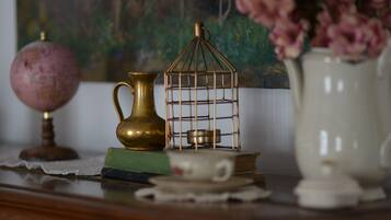 A wooden desk with a globe, a brass birdcage, a vase with pink flowers, and a white pitcher.