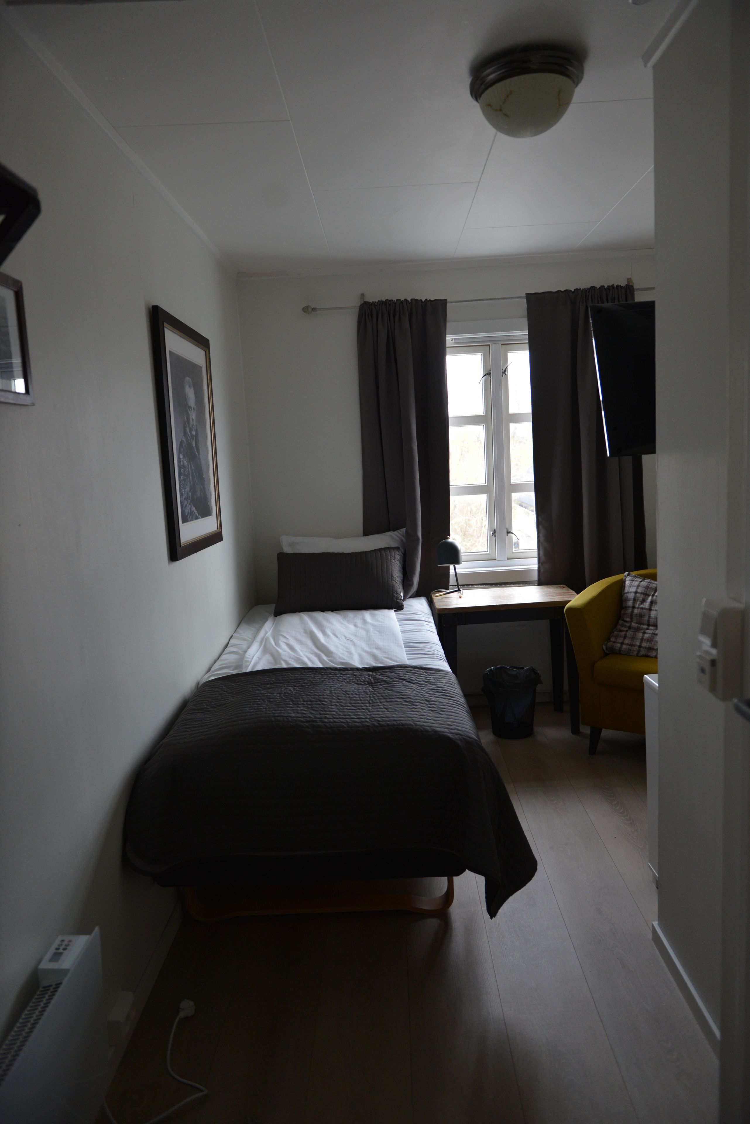 A compact hotel room with a single bed, a desk, a chair, and a window with curtains.