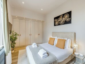 Et hotelværelse med en seng, et natbord, en lampe, en potteplante og et klædeskab.