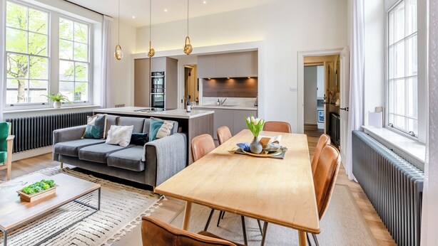 Una cocina moderna con una isla central, comedor con mesa y sillas de madera, y un rincón de estar acogedor con sofá.